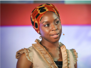 Woman in colorful headwrap sharing personal narrative on stage.