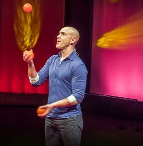Man in blue shirt juggling oranges during a TED Talk on mindfulness.